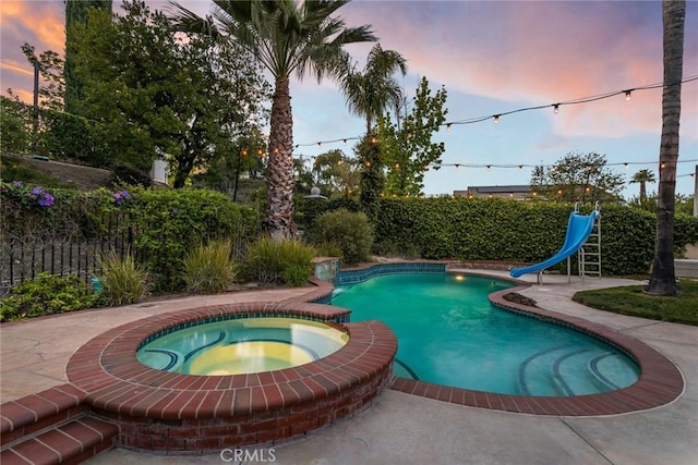 view of swimming pool with a pool with connected hot tub, a water slide, and a fenced backyard