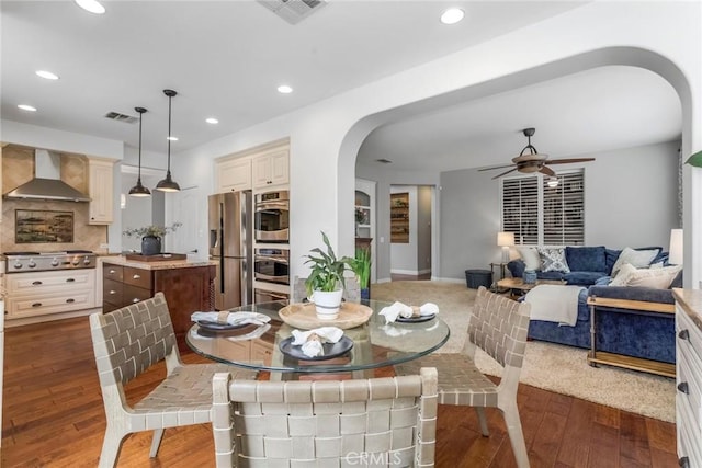 dining room featuring arched walkways, ceiling fan, visible vents, and dark wood finished floors