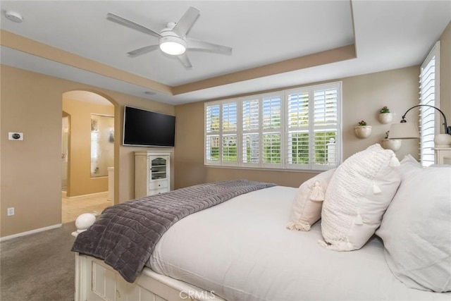 bedroom with ceiling fan, arched walkways, baseboards, carpet floors, and a raised ceiling