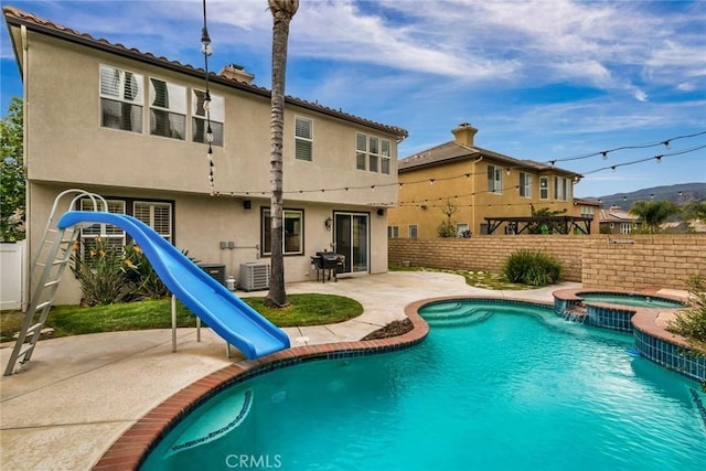 view of swimming pool featuring fence, cooling unit, a patio, a water slide, and a pool with connected hot tub