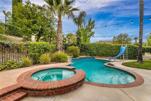 view of swimming pool with fence, a pool with connected hot tub, a water slide, and a patio