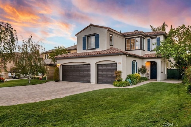 mediterranean / spanish-style house with a tiled roof, a lawn, a garage, decorative driveway, and stucco siding