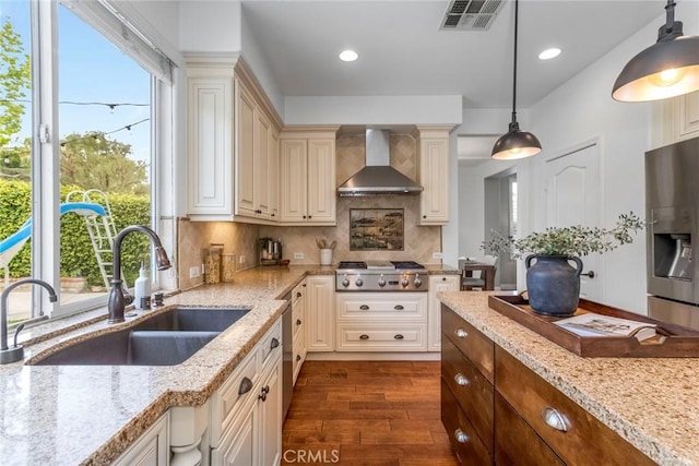 kitchen with visible vents, dark wood-style floors, wall chimney exhaust hood, a sink, and stainless steel appliances