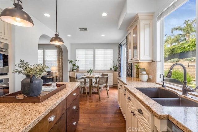 kitchen featuring dark wood-style flooring, a sink, arched walkways, visible vents, and glass insert cabinets
