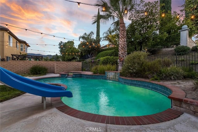 view of pool featuring fence, a pool with connected hot tub, and a water slide
