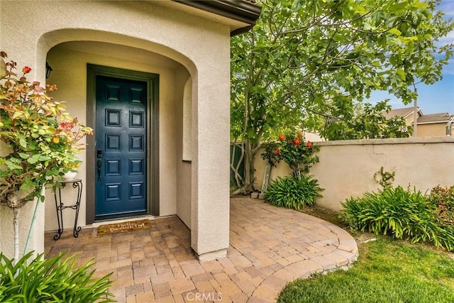 view of exterior entry with fence and stucco siding