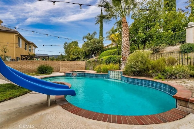 view of pool featuring a water slide, a pool with connected hot tub, and fence