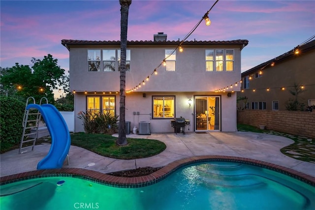 back of house at dusk with a fenced backyard, a patio area, stucco siding, and an outdoor pool