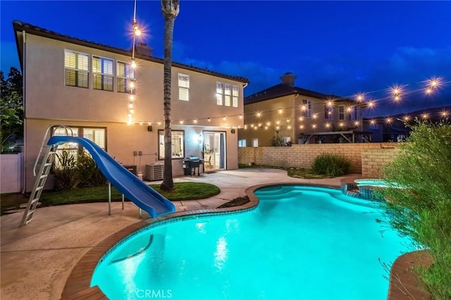 pool at night featuring french doors, a pool with connected hot tub, fence private yard, a patio area, and a water slide