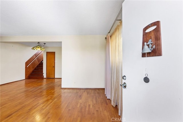 spare room with light wood-type flooring, baseboards, and stairway