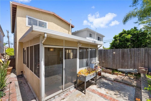 rear view of property with fence, a patio area, a sunroom, and stucco siding