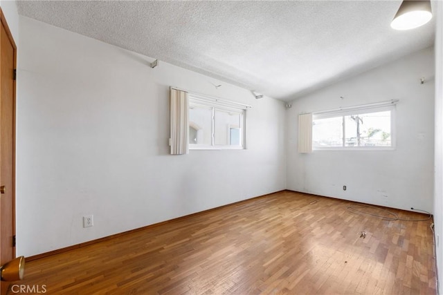 empty room with a textured ceiling, baseboards, wood finished floors, and lofted ceiling