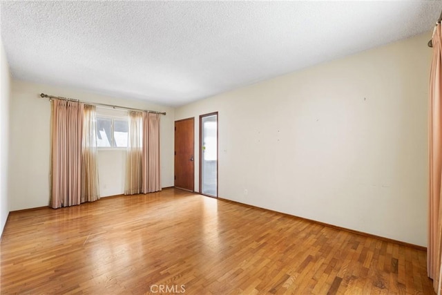 unfurnished room with a textured ceiling, baseboards, and light wood finished floors