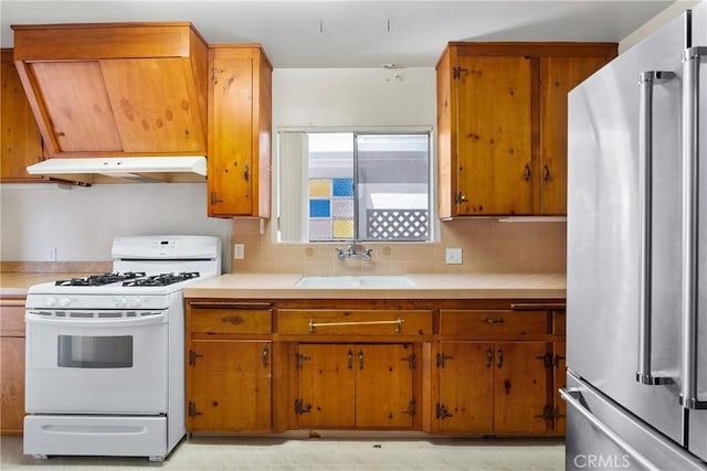 kitchen with white range with gas stovetop, high quality fridge, light countertops, under cabinet range hood, and a sink