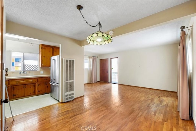kitchen featuring freestanding refrigerator, a heating unit, brown cabinetry, and a wealth of natural light