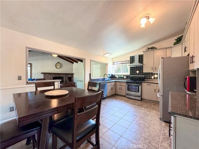 kitchen featuring a sink, wall chimney exhaust hood, stainless steel appliances, lofted ceiling, and backsplash