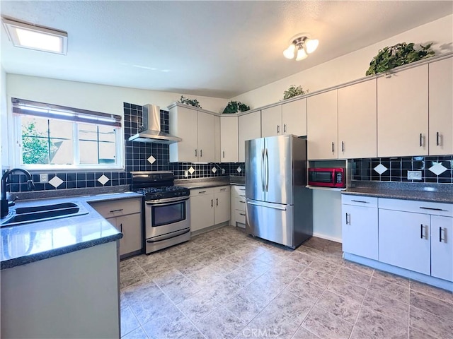 kitchen featuring wall chimney range hood, dark countertops, appliances with stainless steel finishes, a sink, and tasteful backsplash