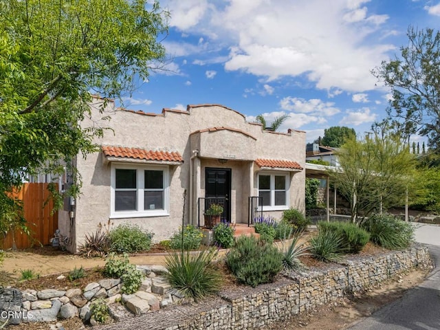 mediterranean / spanish home with fence, a tile roof, and stucco siding