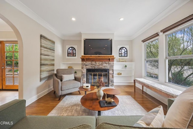 living room featuring crown molding, a brick fireplace, baseboards, recessed lighting, and arched walkways
