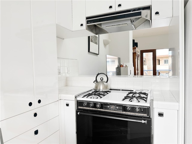 kitchen with tile counters, white cabinetry, backsplash, under cabinet range hood, and range with gas cooktop