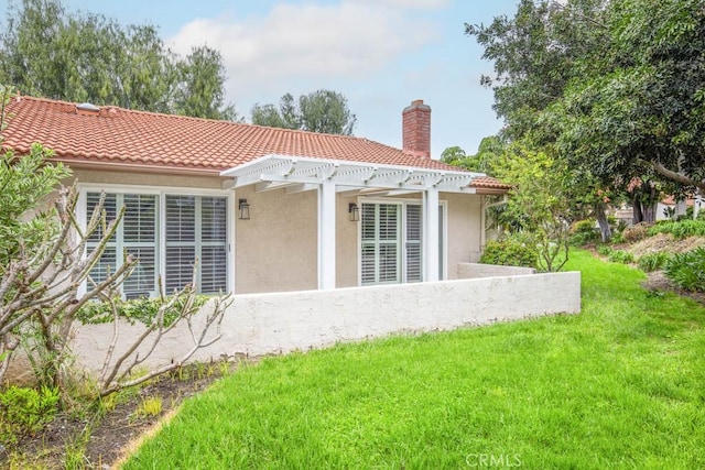 rear view of house featuring a tiled roof, a chimney, a lawn, a pergola, and stucco siding