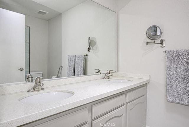 full bathroom with double vanity, toilet, visible vents, and a sink
