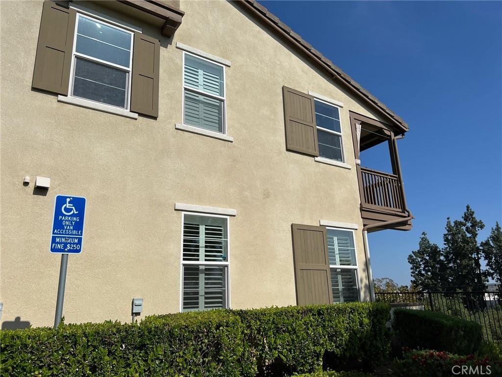 view of side of property with fence, a balcony, and stucco siding