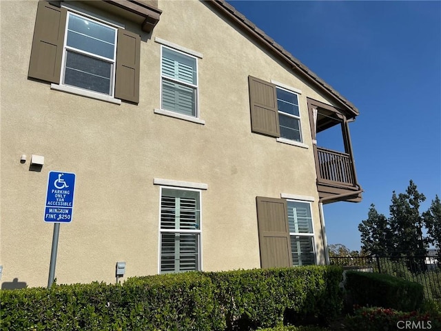 view of side of property with fence, a balcony, and stucco siding