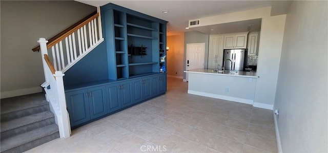 kitchen with a sink, freestanding refrigerator, baseboards, light tile patterned floors, and visible vents