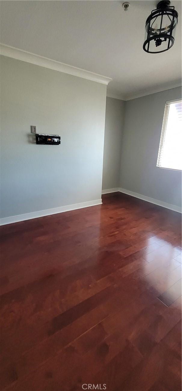 spare room featuring baseboards, ornamental molding, a chandelier, and dark wood-style floors