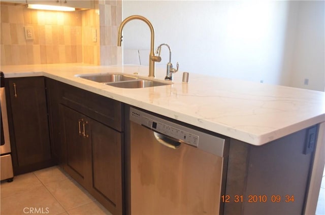 kitchen featuring tasteful backsplash, stainless steel dishwasher, light stone countertops, a sink, and light tile patterned floors
