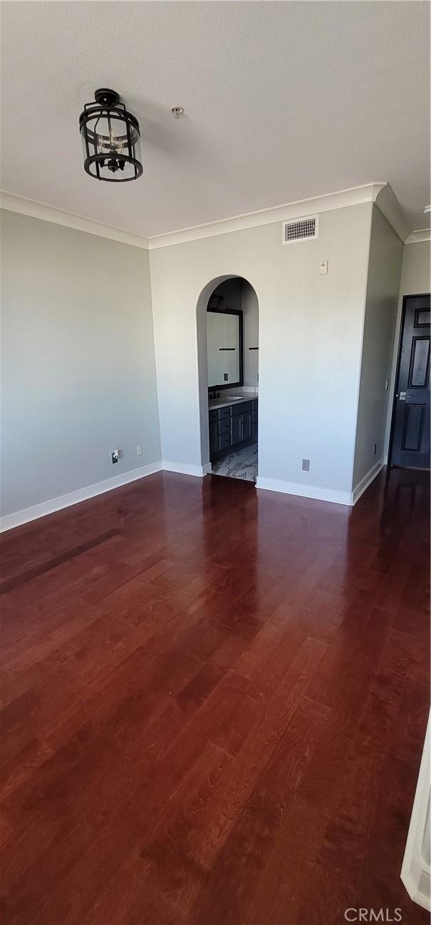 unfurnished room featuring visible vents, arched walkways, wood finished floors, baseboards, and ornamental molding