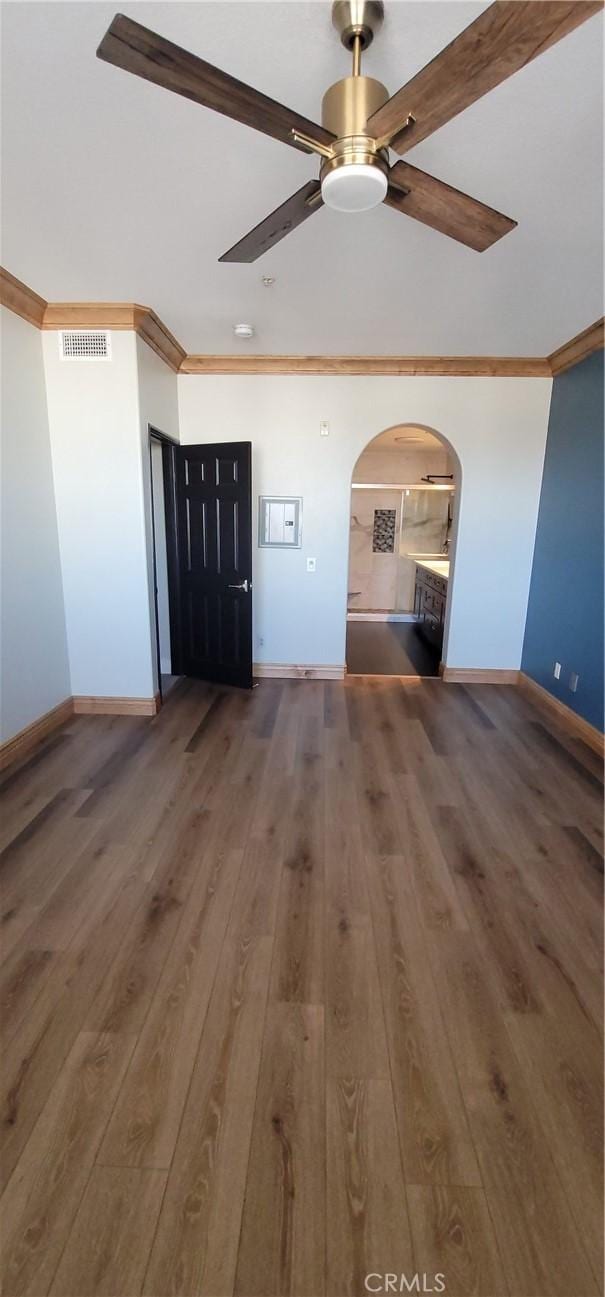 unfurnished living room featuring crown molding, visible vents, hardwood / wood-style floors, baseboards, and arched walkways