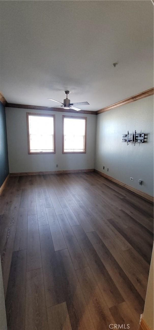 empty room with crown molding, a ceiling fan, dark wood-style flooring, and baseboards