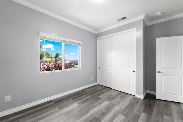 unfurnished bedroom with visible vents, crown molding, a closet, wood finished floors, and baseboards