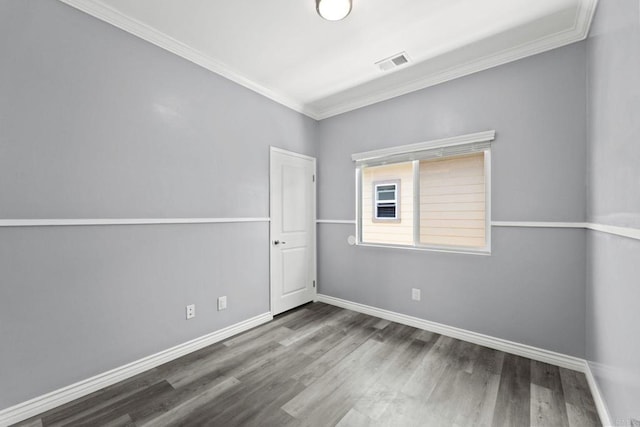 empty room featuring baseboards, visible vents, ornamental molding, and wood finished floors