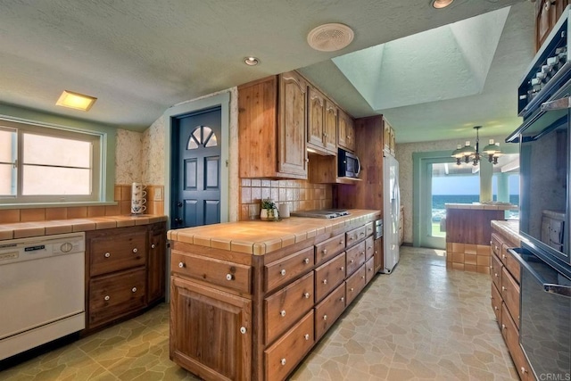 kitchen featuring brown cabinetry, tile countertops, white appliances, and tasteful backsplash