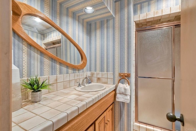 bathroom with wallpapered walls, a shower with shower door, and vanity
