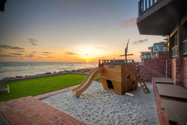 playground at dusk with a lawn, a water view, a patio area, and a playground