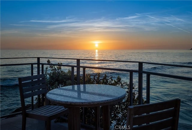 balcony at dusk featuring a water view