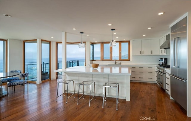 kitchen featuring a kitchen bar, light countertops, wall chimney exhaust hood, dark wood finished floors, and premium appliances