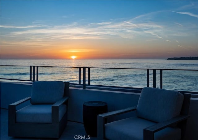 balcony at dusk featuring a water view
