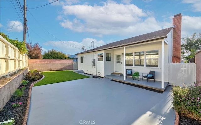 rear view of property featuring covered porch, a fenced backyard, stucco siding, a chimney, and a yard