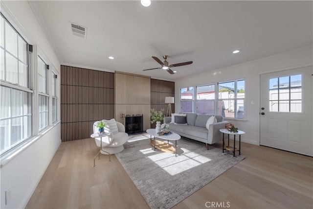 living area featuring visible vents, ornamental molding, light wood finished floors, and ceiling fan