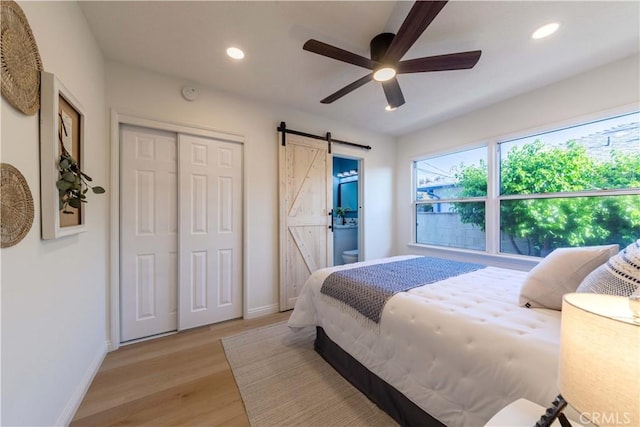 bedroom with recessed lighting, baseboards, light wood-type flooring, and a barn door