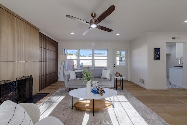 living room featuring crown molding, ceiling fan, visible vents, and light wood-style flooring