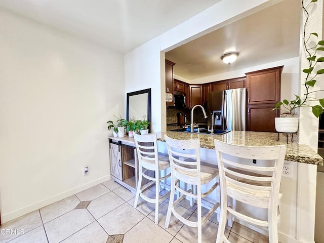 kitchen featuring appliances with stainless steel finishes, a sink, a peninsula, baseboards, and light tile patterned floors