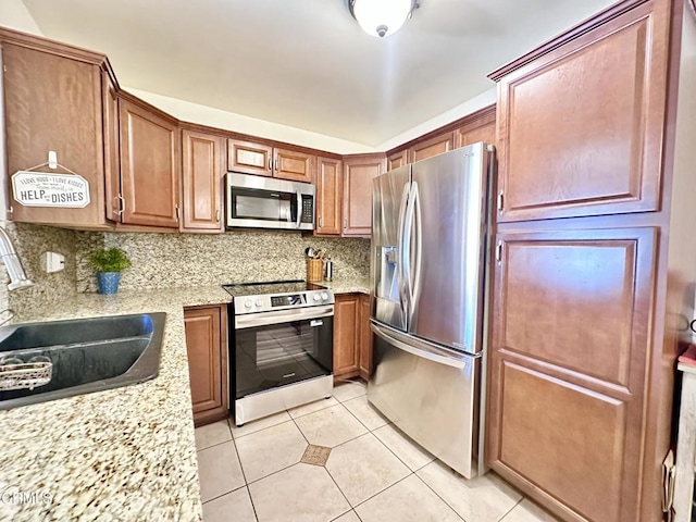 kitchen featuring light tile patterned flooring, light stone countertops, a sink, stainless steel appliances, and backsplash
