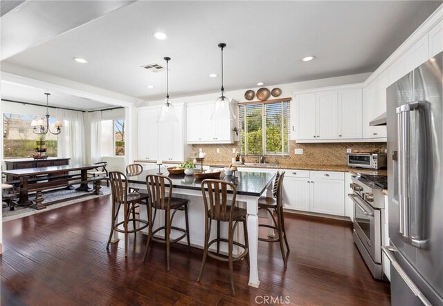 13216 Finish Draft Ct, Eastvale, CA 92880 - kitchen featuring high end appliances, tasteful backsplash, dark wood-style flooring, white cabinetry, and wall chimney range hood