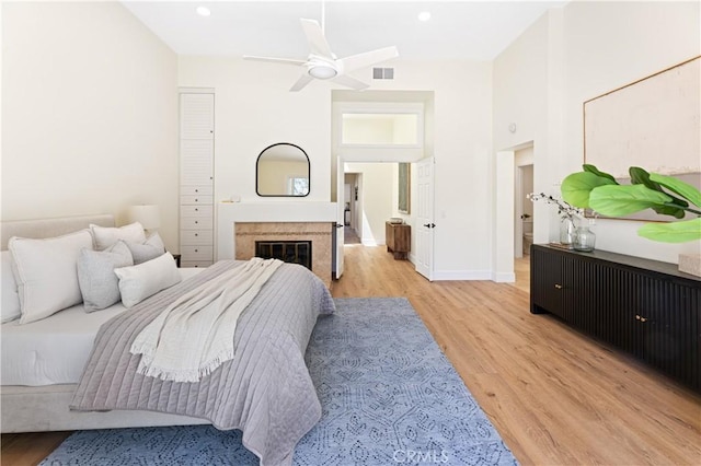 bedroom featuring visible vents, light wood-type flooring, baseboards, a glass covered fireplace, and recessed lighting